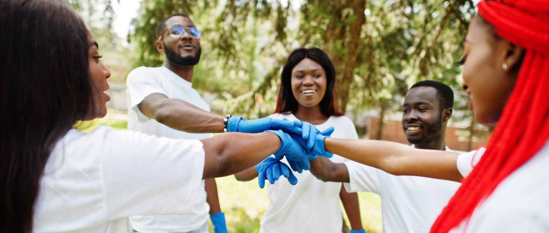 Group of happy african volunteers put hands in hands in park. Africa volunteering, charity, people and ecology concept.